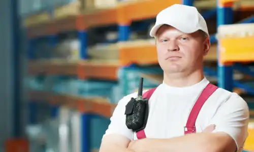 A muscular worker in a safety helmet standing with arms crossed.